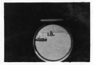 Two boats on the water in the Hong Kong harbor, one Chinese junk and one metal ship. Image taken from ship porthole.